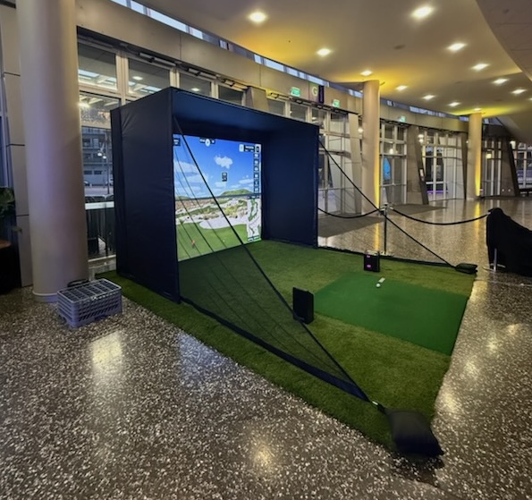 The Fairway Finder pop-up golf simulator set up indoors, with enclosure, big screen and turf hitting area